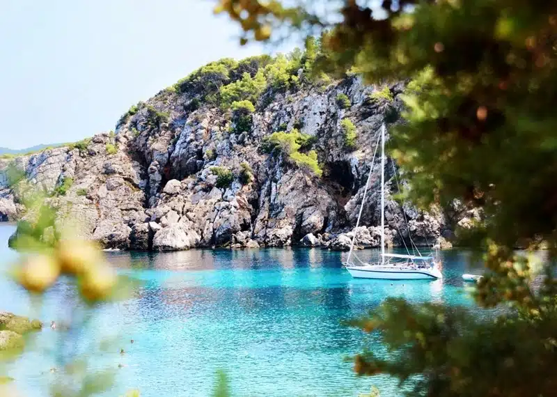 Charter boat anchored in a secluded rocky cove with crystal-clear turquoise water framed by coastal vegetation
